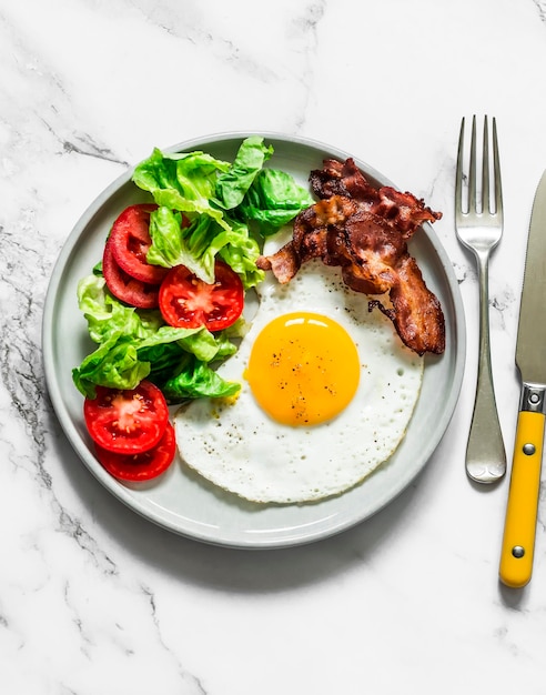 Assiette de petit déjeuner œuf frit bacon et salade de légumes sur fond de marbre clair vue de dessus