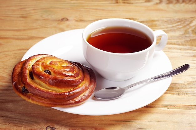 Assiette avec petit pain frais et tasse de thé chaud sur une table en bois rustique