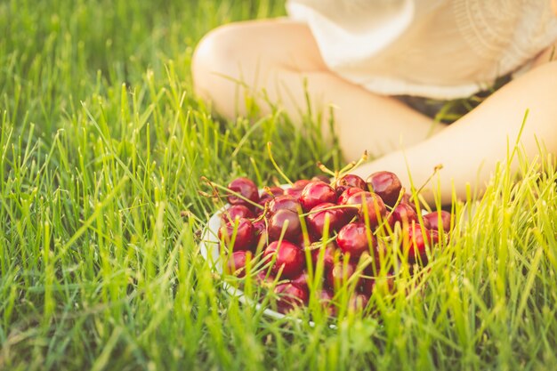 Une assiette pleine de cerises se dresse sur l'herbe aux pieds d'un enfant assis