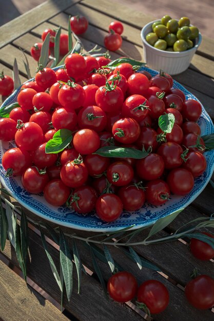 Assiette pleine de tomates cerises mûres sur une table en bois au soleil
