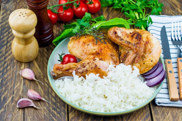 Une assiette de poulet frit grillé et de riz bouilli. tomates, feuilles de coq, ail sur une planche de bois. fond en bois rustique.