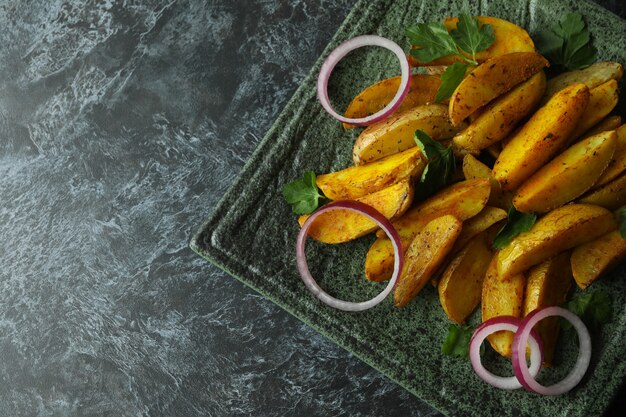 Assiette avec quartiers de pommes de terre, persil et oignon sur fond noir fumé