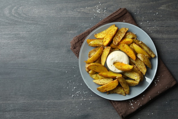 Assiette avec quartiers de pommes de terre et sauce sur fond texturé foncé