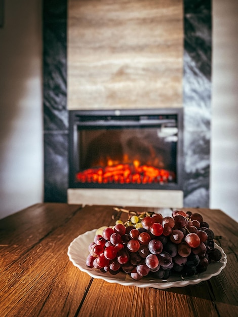 Assiette de raisins violets posée sur une table en bois devant une cheminée dans un cadre cosy