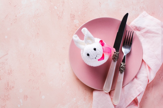 Assiette rose, couverts, serviette et lapin blanc, symbole de la serviette de Pâques sur la vue de dessus de table en pierre