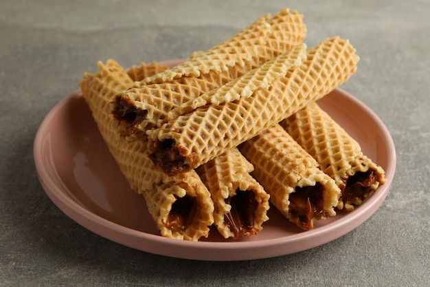 Assiette avec des rouleaux de gaufrette avec du lait condensé sur gris