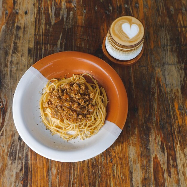 Assiette saine de spaghettis italiens garnie d'une savoureuse sauce bolognaise à la tomate et au bœuf haché et de basilic frais sur une table en bois brun rustique Servie avec cappuccino