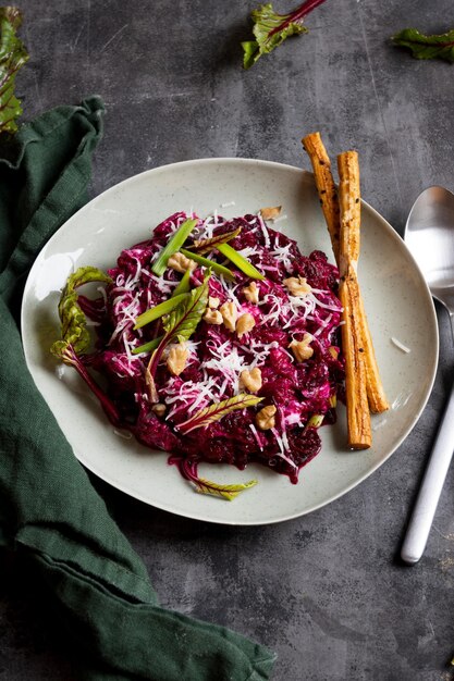 Une assiette de salade de betteraves rouges avec des haricots verts et une cuillère sur fond sombre.