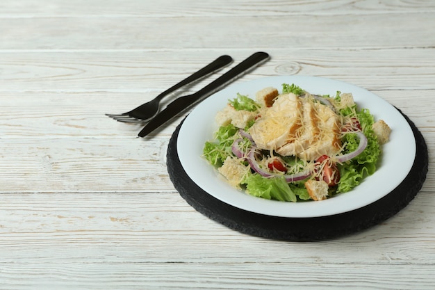 Assiette avec salade César et couverts sur table en bois blanc