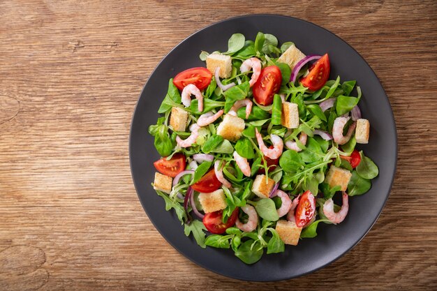 Assiette de salade fraîche aux verts de crevettes et tomates sur une table en bois