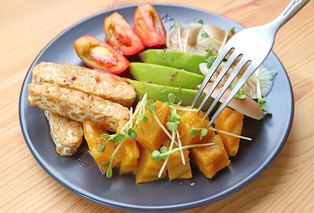 Assiette de salade de légumes colorés au tempeh poêlé garnie de pousses de daikon