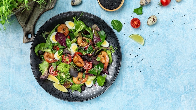 Assiette de salade saine. Recette de fruits de mer frais. tomates cerises, concombre, avocat, oeufs et crevettes fumées, mesclun. Format de bannière longue, vue de dessus.