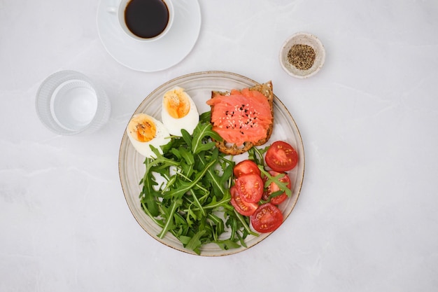 Une assiette avec un sandwich au saumon tomates roquette œuf à la coque avec un verre de café et de verre