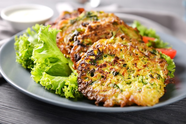 Assiette avec de savoureuses crêpes aux courgettes sur table en bois, gros plan