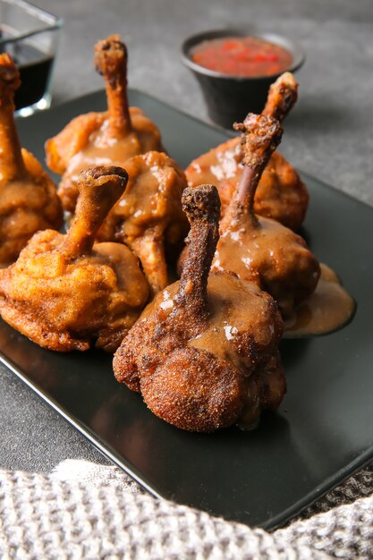 Assiette avec de savoureuses sucettes au poulet sur une surface sombre