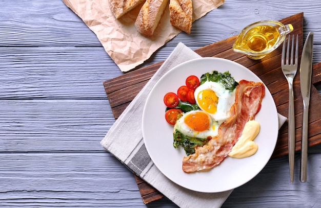 Assiette avec de savoureux œufs épinards et bacon sur table en bois