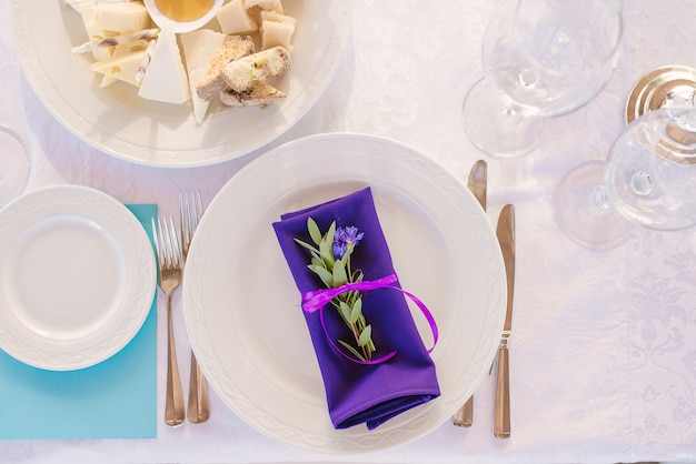 Assiette de service avec des couverts et une serviette de table violette avec un brin d'eucalyptus dans le décor d'un dîner de mariage ou de vacances