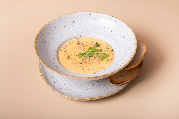 Une assiette de soupe à la crème au fromage avec des noix et des légumes verts sur un fond beige.