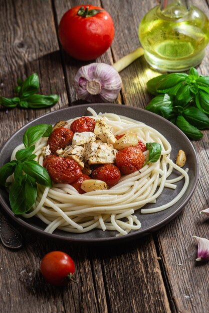 Une assiette de spaghettis au poulet et tomates sur une table en bois.