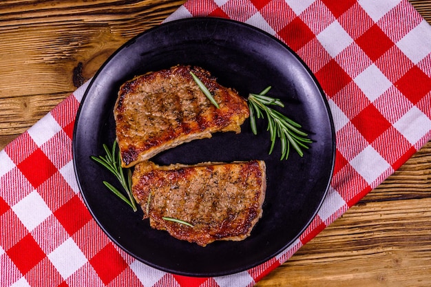 Assiette avec steaks rôtis et brindilles de romarin sur une table en bois Vue de dessus