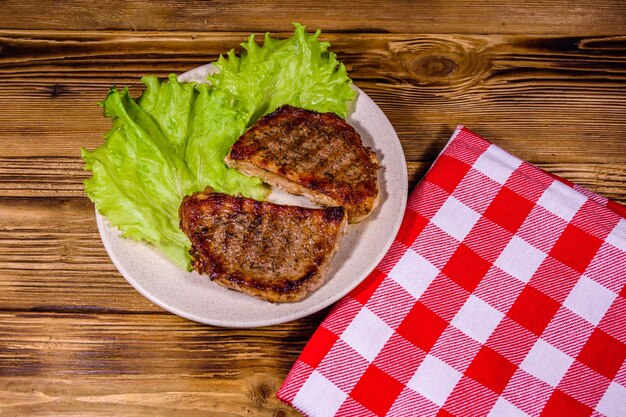 Assiette avec steaks rôtis et brindilles de romarin sur une table en bois