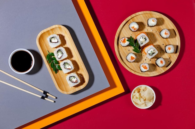 Une assiette de sushis et un bol de trempette sont posés sur un fond rouge.