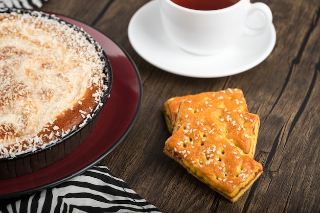 Assiette de tarte sucrée avec pépites de noix de coco, tasse de thé et biscuits sur une surface en bois