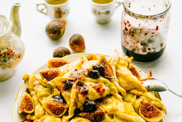 Une assiette avec des tartes et des figues sur la table, des appareils de cuisine, un pot de confiture ouvert, un service à thé