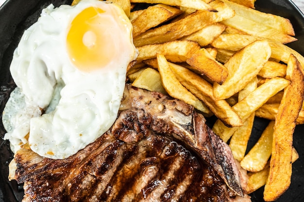 Photo assiette avec un tbone grillé ou au barbecue accompagné d'une portion de frites et d'un œuf au plat vue de dessus concept de cuisine traditionnelle faite maison gros plan