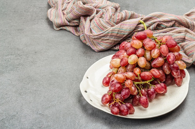 Assiette tendance avec une grappe de raisins roses Serviette textile vintage Pierre fond béton