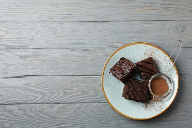 Assiette avec des tranches de gâteau au chocolat et passoire avec de la poudre sur fond de bois, espace pour le texte