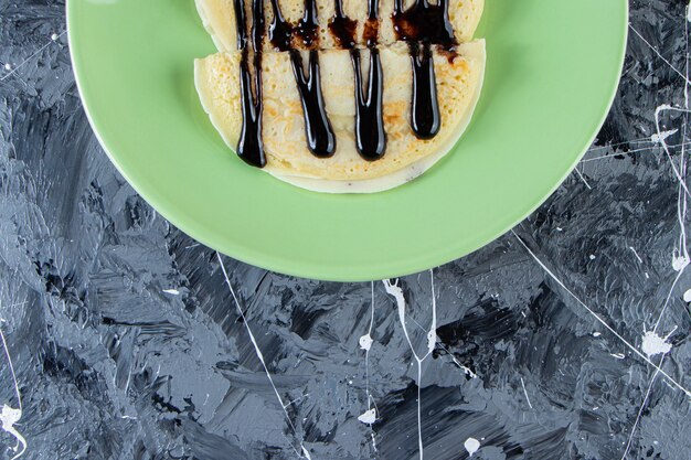 Assiette verte de crêpes maison avec garniture au chocolat sur une surface en marbre.