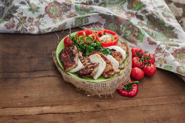 Une assiette de viande cuite, de fromage et de légumes rouges sur une table en bois. Nappe textile proche avec ornement vintage