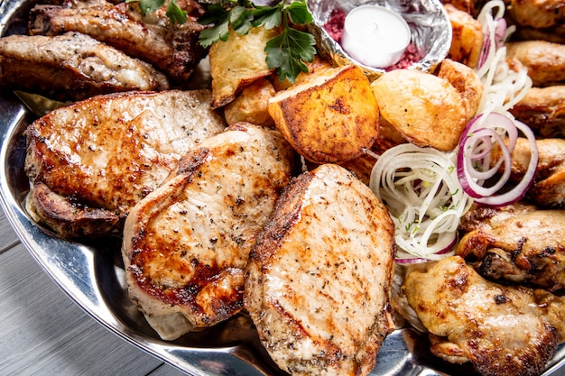 Photo assiette de viande avec de délicieux morceaux de viande, pommes de terre, oignons et bougies sur une table en bois blanche