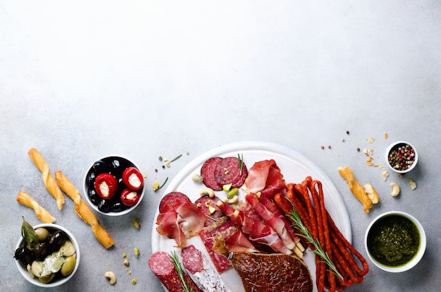 Assiette de viande fumée à froid. Antipasti traditionnel italien, planche à découper avec salami, prosciutto, jambon, côtelettes de porc, olives sur fond gris. Vue de dessus, espace de copie, pose à plat