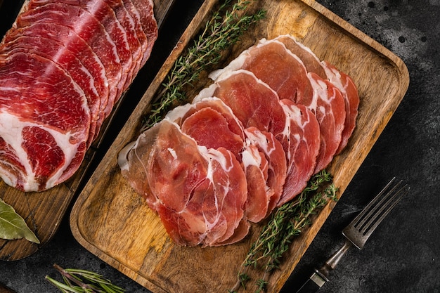 Assiette de viande fumée froide avec prosciutto, salami, bacon, sur fond de table en pierre noire noire, vue de dessus à plat