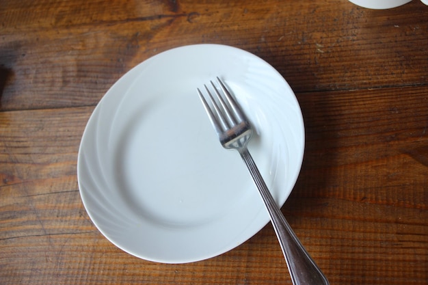 Assiette vide blanche avec fourchette sur une vieille planche de bois sur un fond en bois foncé