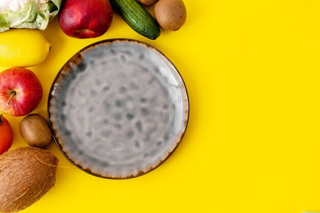 Assiette Vide En Céramique Grise Vue De Dessus Sur Fond Jaune. Beaucoup De Fruits Et Légumes. Nourriture Végétalienne