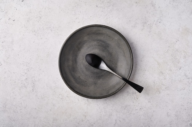 Assiette vide et cuillère ustensiles de cuisine sombres sur table gris clair vue de dessus à plat avec copie