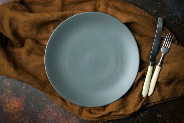 Assiette vide sur fond sombre. Assiette en céramique grise vide avec un couteau et une fourchette pour la nourriture et le dîner sur un beau fond sombre.