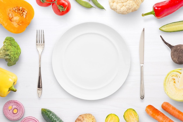 Assiette vide fourchette et couteau entouré de légumes mise à plat close up