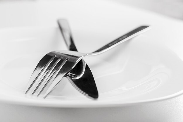 Assiette vide, fourchette et couteau se trouvent en travers sur un fond blanc.