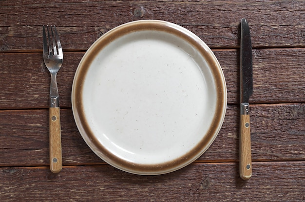 Assiette vide fourchette et couteau de table sur la vieille table en bois