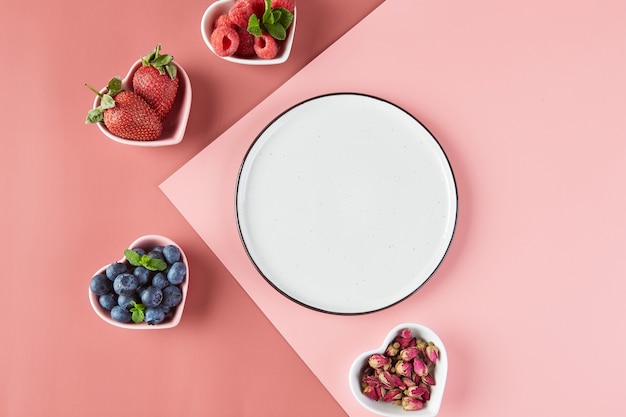 Assiette vide et petites assiettes en forme de coeurs avec fraises fraîches framboises myrtilles, vue de dessus