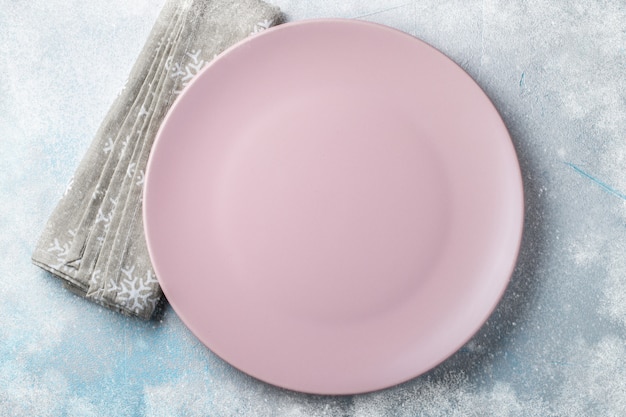 Assiette vide rose avec des couverts et une serviette beige.