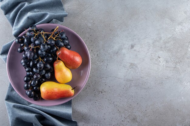 Assiette violette de raisins noirs frais et de poires sur la surface de la pierre