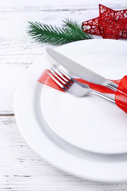 Assiettes blanches, couteau, fourchette, serviette et décoration de Noël sur table en bois