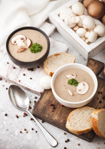 Assiettes en bol en céramique de soupe crémeuse aux champignons et châtaignes avec cuillère poivre et torchon sur fond de cuisine blanc et boîte de champignons crus Vue de dessus