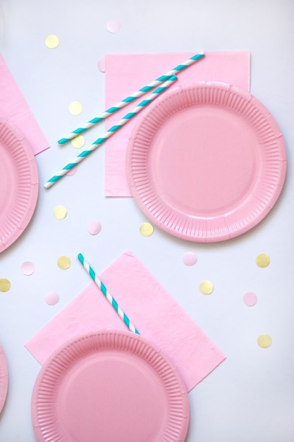 Assiettes jetables en papier rose serviette et pailles pour boissons sur fond blanc avec des confettis Table pour pique-nique Ecocourt lumineux Fête d'anniversaire et concept de vacances Vue de dessus à plat