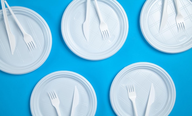 Assiettes en plastique blanc fourchettes et couteaux sur fond bleu